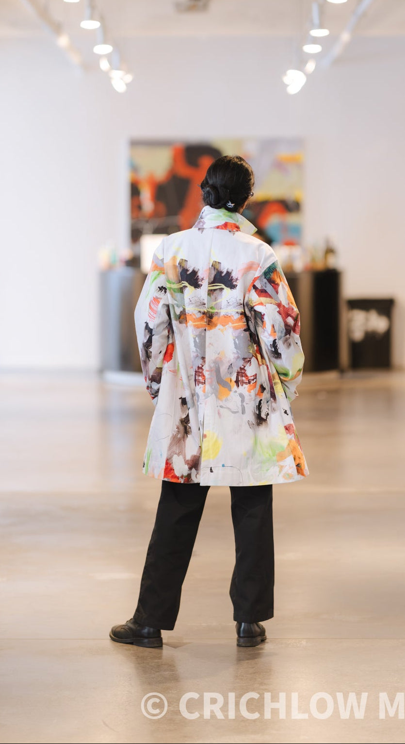 The back of the ModaMichelle Splatter Print Car coat, standing in a bright art gallery with white walls and ceiling lights.